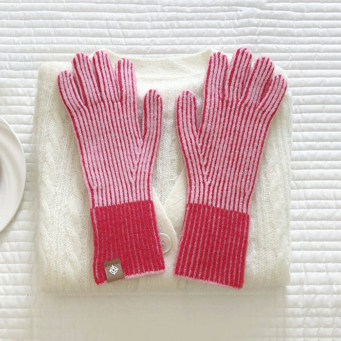 Flat lay contrast striped knit gloves in red and white with ribbed cuffs, styled on a sweater; cozy winter wear.