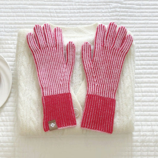 Flat lay contrast striped knit gloves in red and white with ribbed cuffs, styled on a sweater; cozy winter wear.