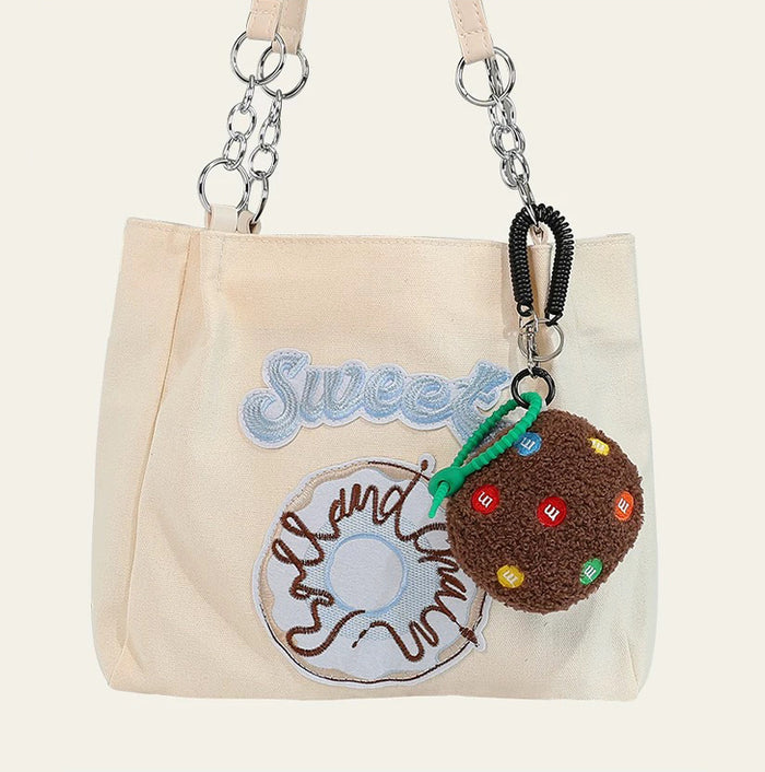 Dark brown Cookie Bag Charm hanging on a tote bag, easy to attach to bags and phones.