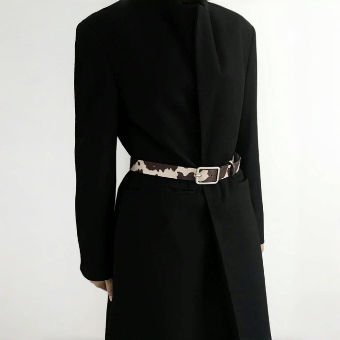 Model wearing a cow print furry belt over a black blazer; chic waist-cinching accessory perfect for office styling.