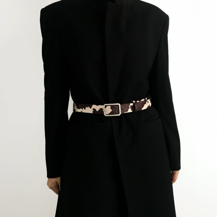 Close-up of cow print belt on a black coat; trendy animal print design suited for winter street style and layering.