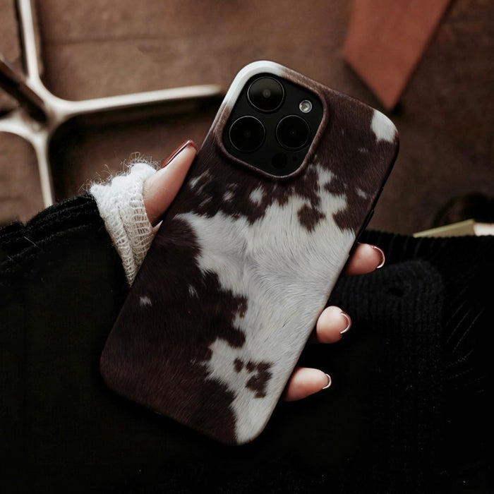 Hand holding brown and white cowhide pattern silicone phone case. Realistic animal print texture for iPhone.