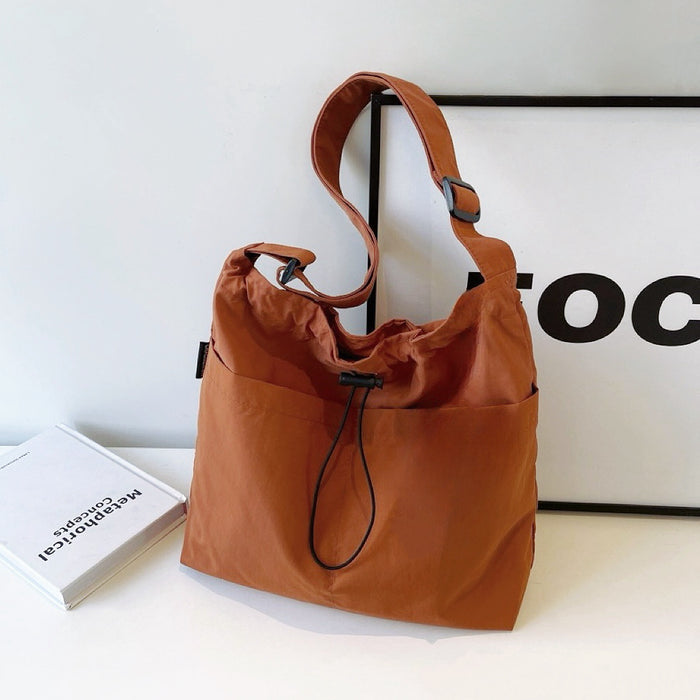 Front view of tan Cozy nylon drawstring bag with adjustable shoulder strap, outer slip pockets, and magnetic.