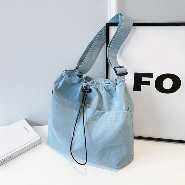Close-up of Light blue nylon drawstring bag with adjustable strap, two outer slip pockets, and black cord closure.