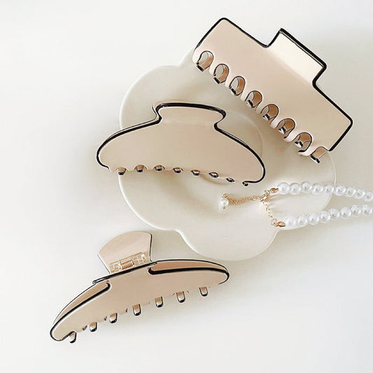 Front view of Three cream acrylic hair claws with black borders in various sizes and shapes.