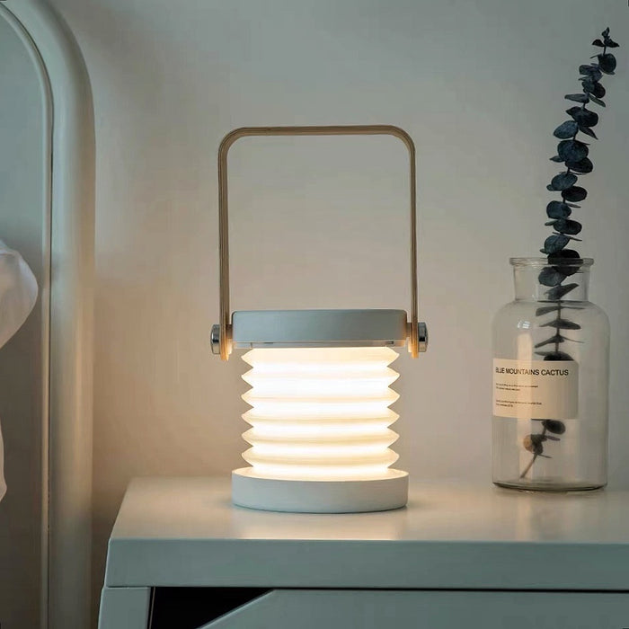 White and wood creative lantern lamp, stretched with glowing accordion light, on a nightstand.