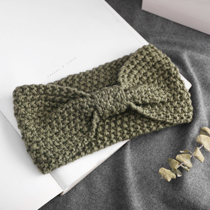 Front view of Olive green  crochet bow headband,on a white book and gray fabric.