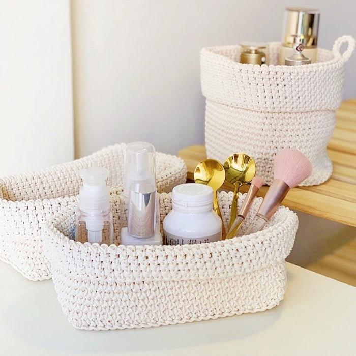 Oval cream polypropylene fiber crochet storage basket holding cosmetics and beauty tools.
