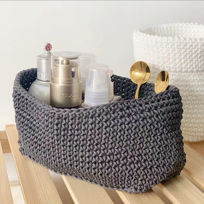 Close-up of grey crochet storage basket with cosmetics and spoons inside, ideal for desk organization.