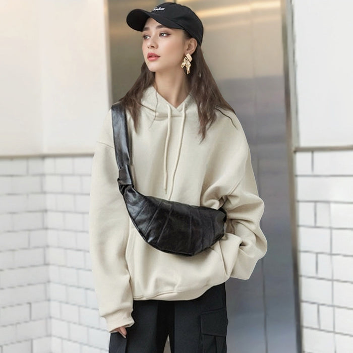 Model wearing black crescent-shaped soft faux leather bag as crossbody featuring minimalist pleated design.