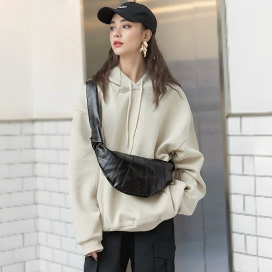 Model wearing black crescent-shaped soft faux leather bag as crossbody featuring minimalist pleated design.