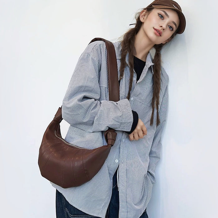 Model wearing the dark brown supple leather shoulder bag with unique pleated construction showcasing sophisticated sculptural aesthetic.