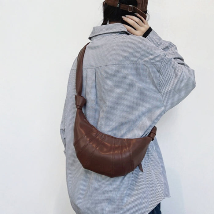 Detailed view of brown faux-leather shoulder bag emphasizing modern crescent silhouette.