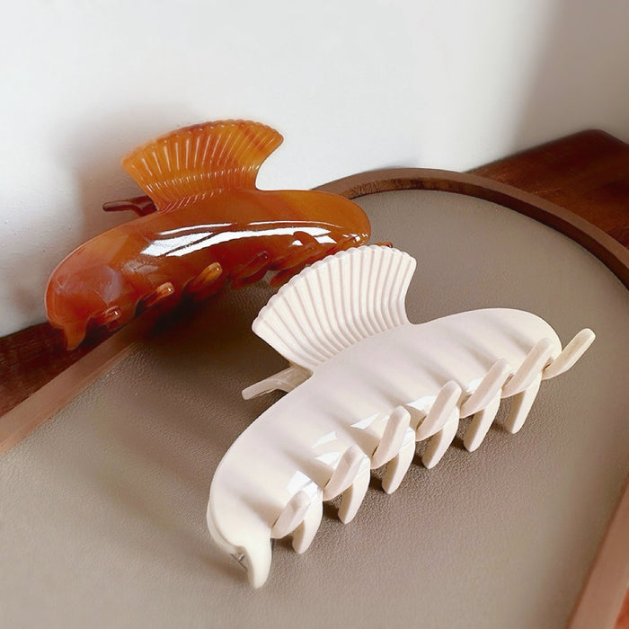 Two acrylic shell hair claws, one glossy brown and one matte cream, with ribbed fan details hair claw.