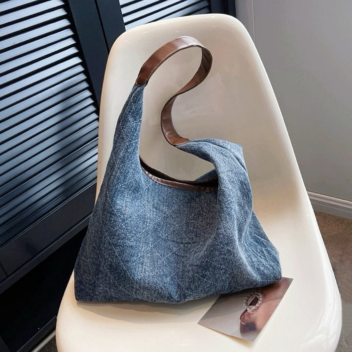 Angled view of dark blue denim shoulder bag with a diamond pattern and brown leather strap.