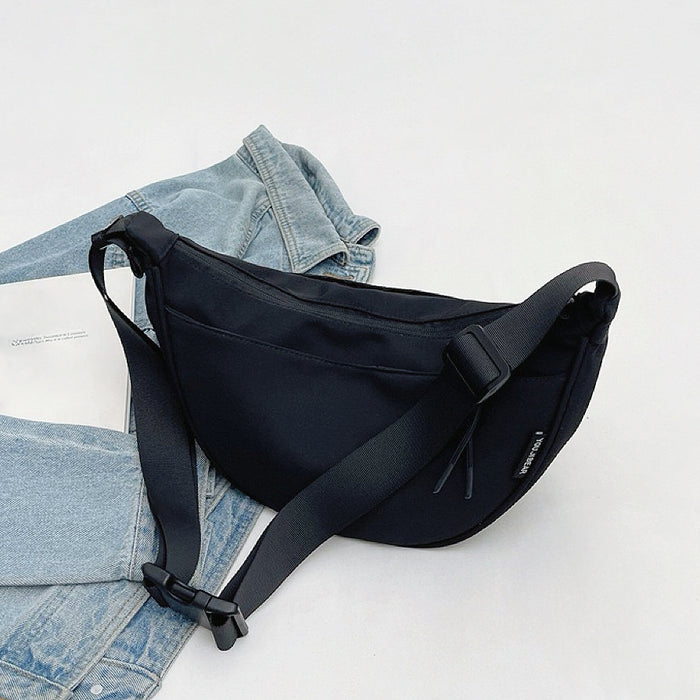 Black nylon crescent crossbody bag lying flat with denim; durable material ideal for casual outfit.