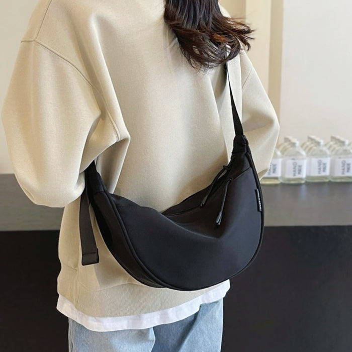 Model wearing a black crescent bag across the back; sleek minimalist silhouette perfect for urban street style.