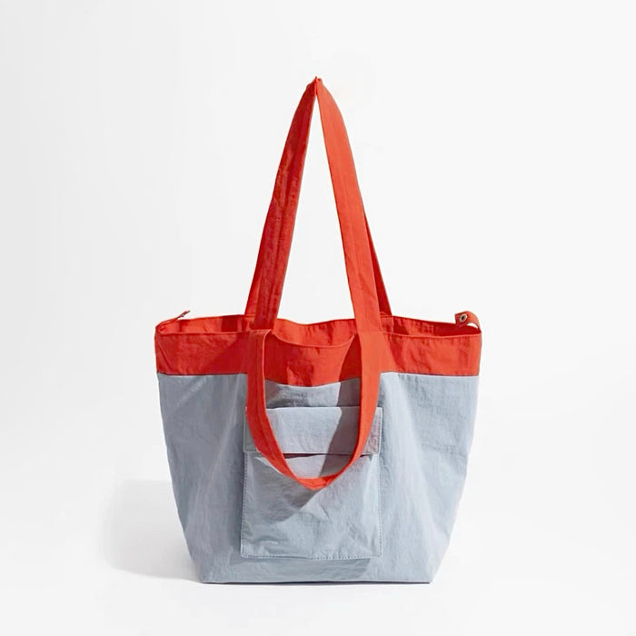 Duotone foldable nylon tote bag in red and light blue with two shoulder straps and a front pocket. ideal for errands.