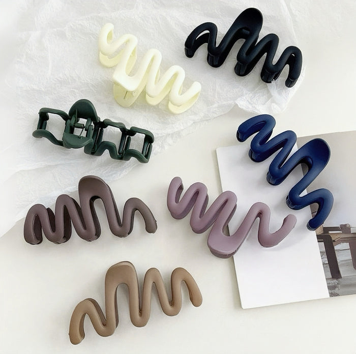 Flat lay of seven acrylic wave hair claws in black, cream, dark khaki, green, navy blue, brown, purple.