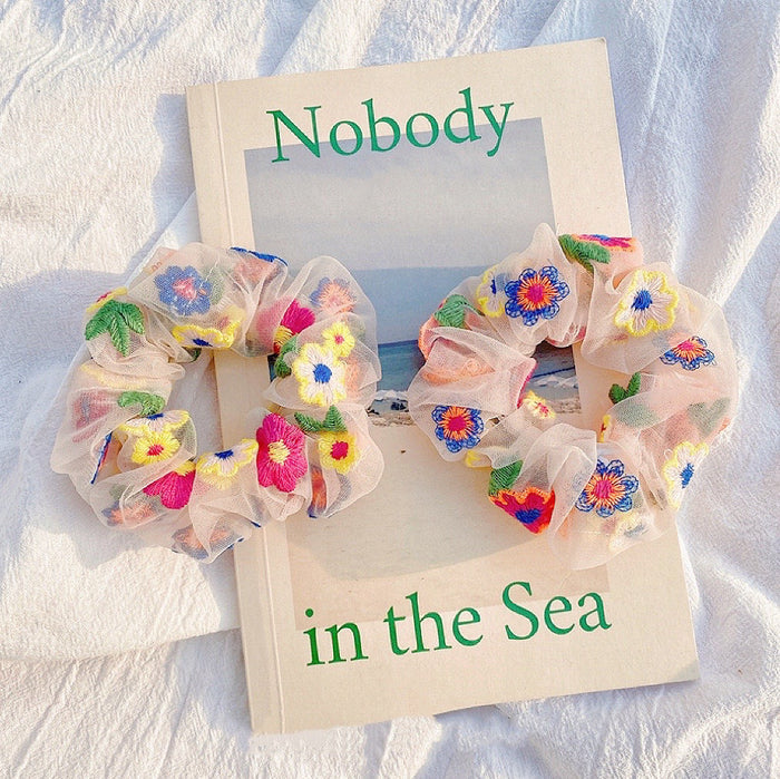 Off-white fabric scrunchie with delicate pink flower embroidery.