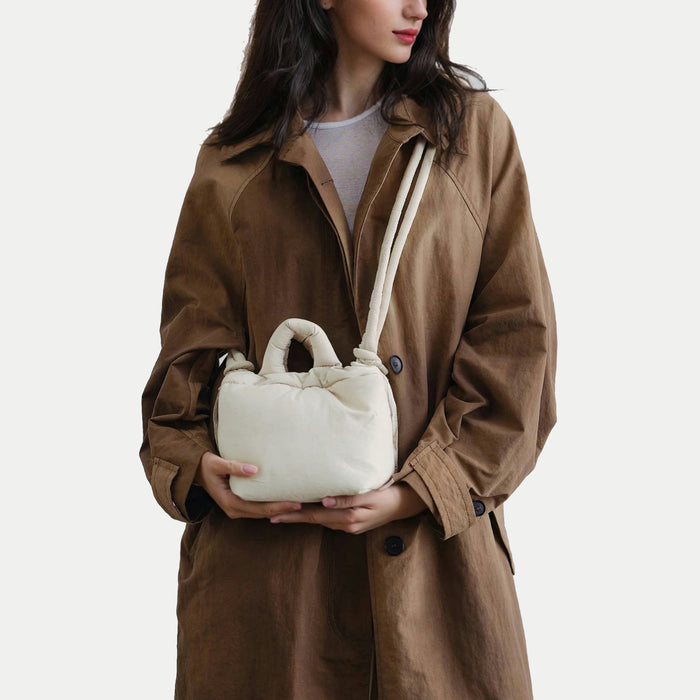 Minimalist cream white padded purse held by hand, demonstrating the hand-twisted carry option for elegant looks.