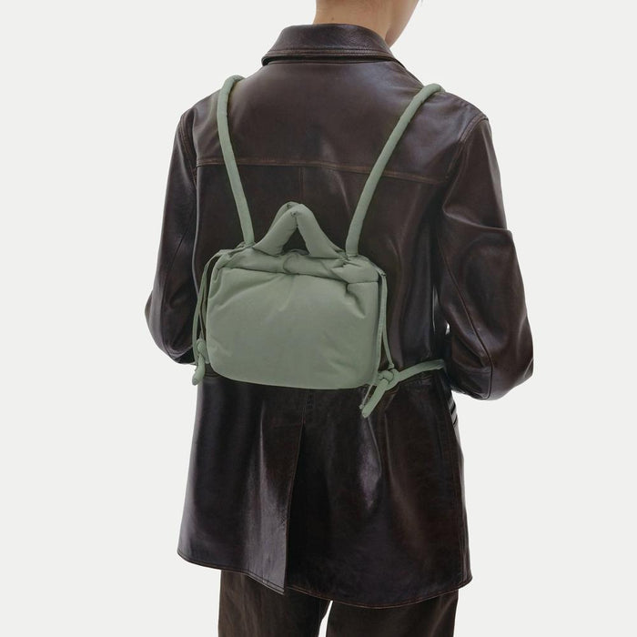 Rear view of model wearing the FlexKnot as a mini backpack, showing the multi-use strap configuration over a leather jacket.