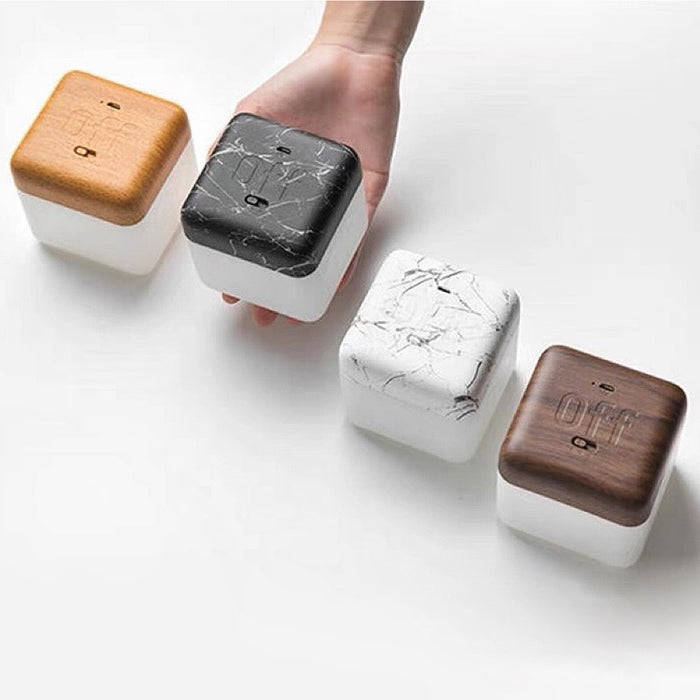 Hand holding a dark marble Flipping Cubic Timer Lamp, with beech wood, white marble, and walnut wood lamps beside it.