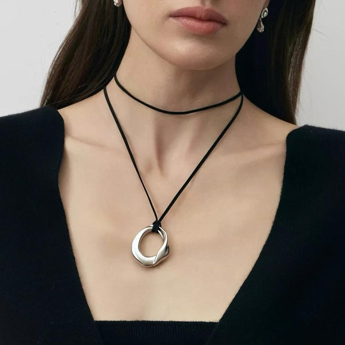 Model wearing silver fluid oval pendant on black leather cord, contemporary artistic jewelry styling
