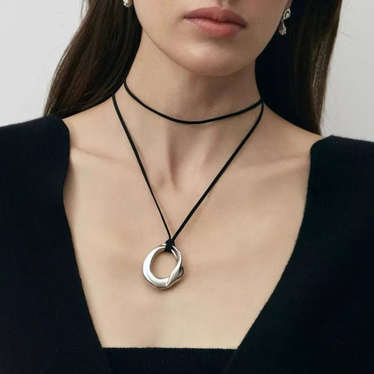 Model wearing silver fluid oval pendant on black leather cord, contemporary artistic jewelry styling