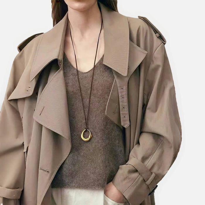 Model wearing gold fluid oval necklace with tan trench coat, sophisticated layering style