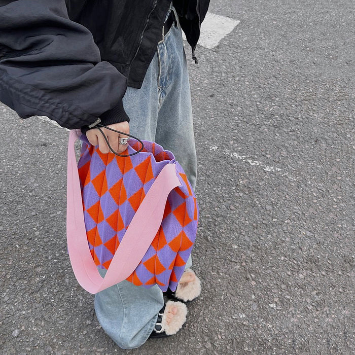 Model holding a vibrant purple and orange argyle knitted tote bag on a city street.
