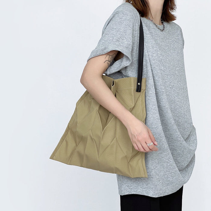 Model wearing khaki pleated bag on shoulder; lightweight fabric perfect for long city walks and sightseeing.