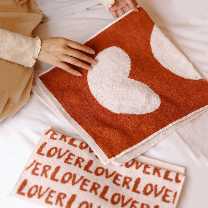 Hands holding a red and white cotton face towel with a large heart design.