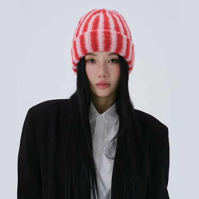 Model wearing a red and pink contrast striped fuzzy beanie with a black blazer.