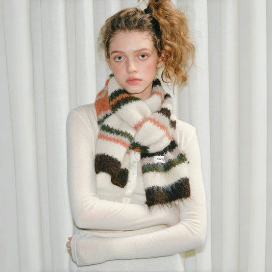 Model wearing Fuzzy wool-polyester striped scarf in earthy tones of cream, brown, green, and orange Fuzzy Nature.