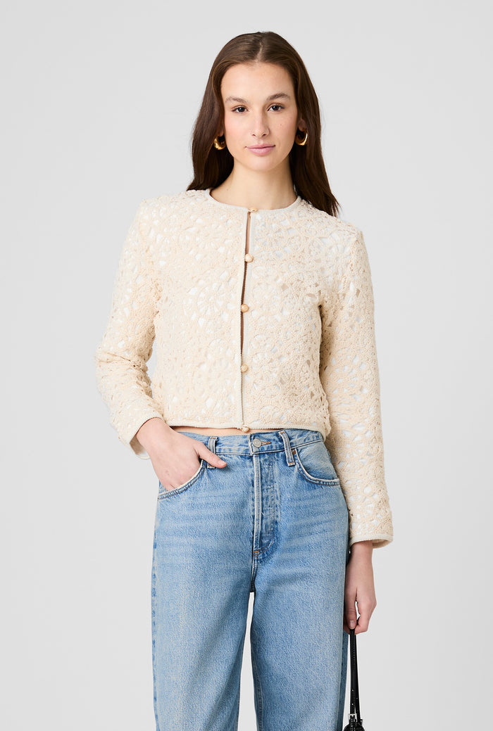 Woman wearing a beige textured jacket and blue jeans on a light gray background