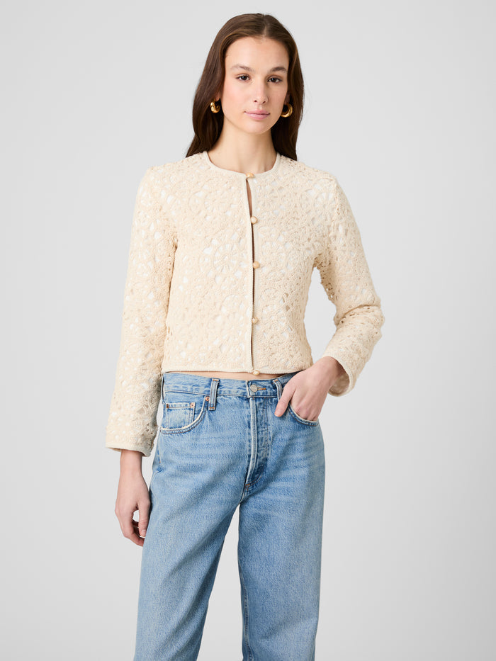 Woman wearing a beige textured jacket and blue jeans on a light gray background