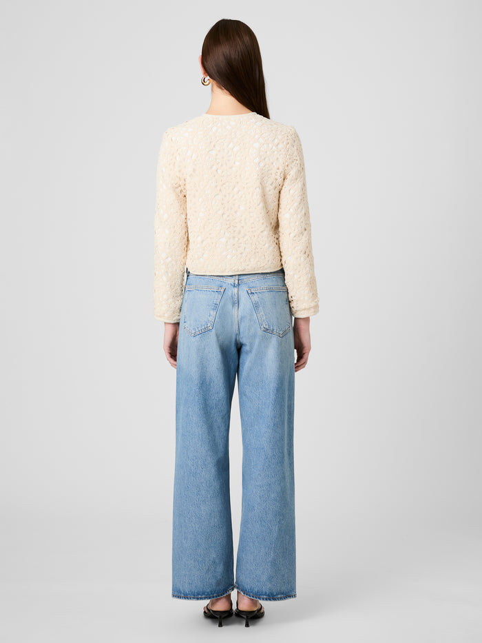 Person wearing a cream sweater and light blue jeans on a plain background
