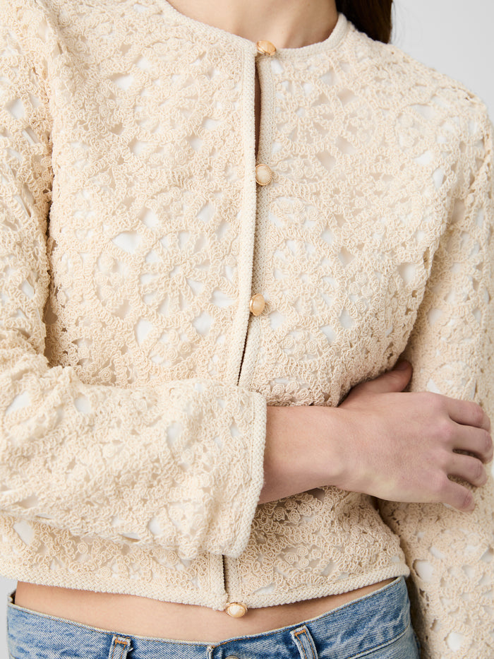 Close-up of a person wearing a beige textured jacket with pearl buttons.