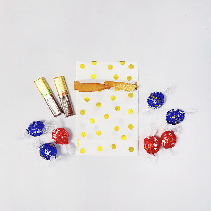 Close-up of White PE gift bag with gold polka dots in and a satin ribbon drawstring closure, surrounded by chocolates.