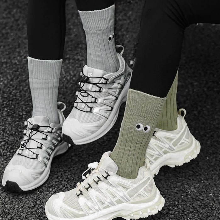 Two models wearing cotton googly eyes socks: one olive green and one grey.