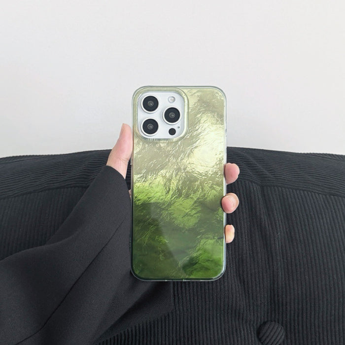 Hand holding green gradient glacier texture case. Cool-toned ripple finish on resilient silicone.