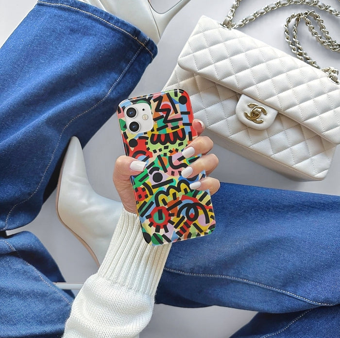 Person in jeans holding graffiti silicone case next to white bag. Edgy lifestyle aesthetic shot.