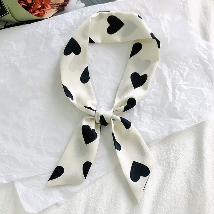 Angled view of White polyester skinny scarf with black heart pattern, tied in a knot in navy, easy for travel packing.