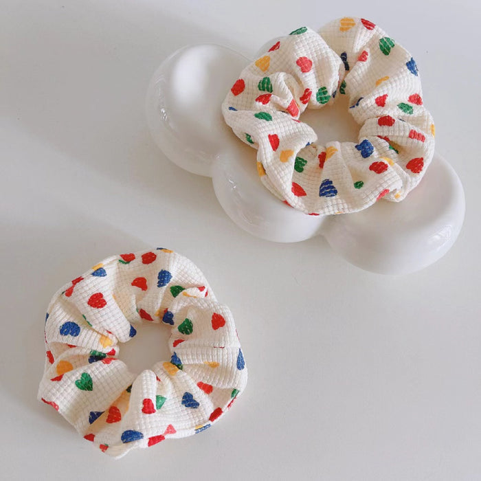 Two white cotton scrunchies with colorful heart prints.