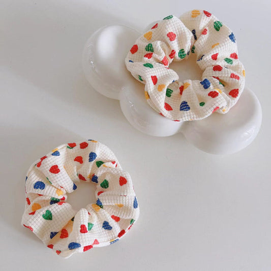 Two white cotton scrunchies with colorful heart prints.