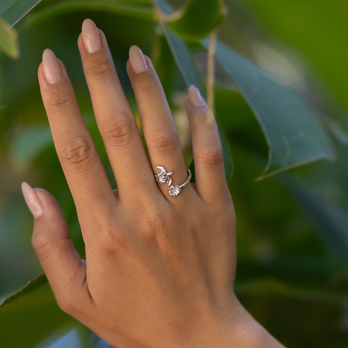 Hand against a large green leaf wearing a Honu and Plumeria Bypass Ring in Sterling Silver