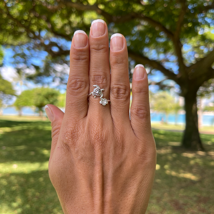 A woman's hand with a Honu and Plumeria Ring in Sterling Silver with a park in the back