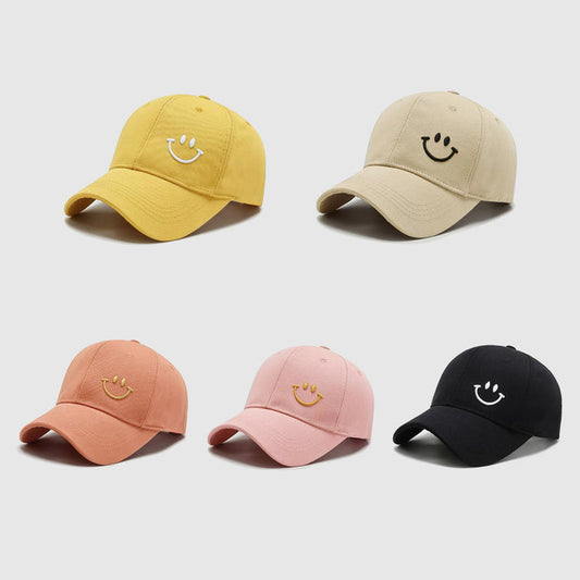 Five cotton Joyful Grin Caps in yellow, beige, peach, pink, and black with embroidered smiley faces for daily fun.