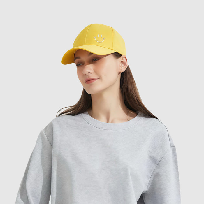 Woman wearing a yellow cotton Joyful Grin Cap with an embroidered smiley face, perfect for a cheerful casual look.